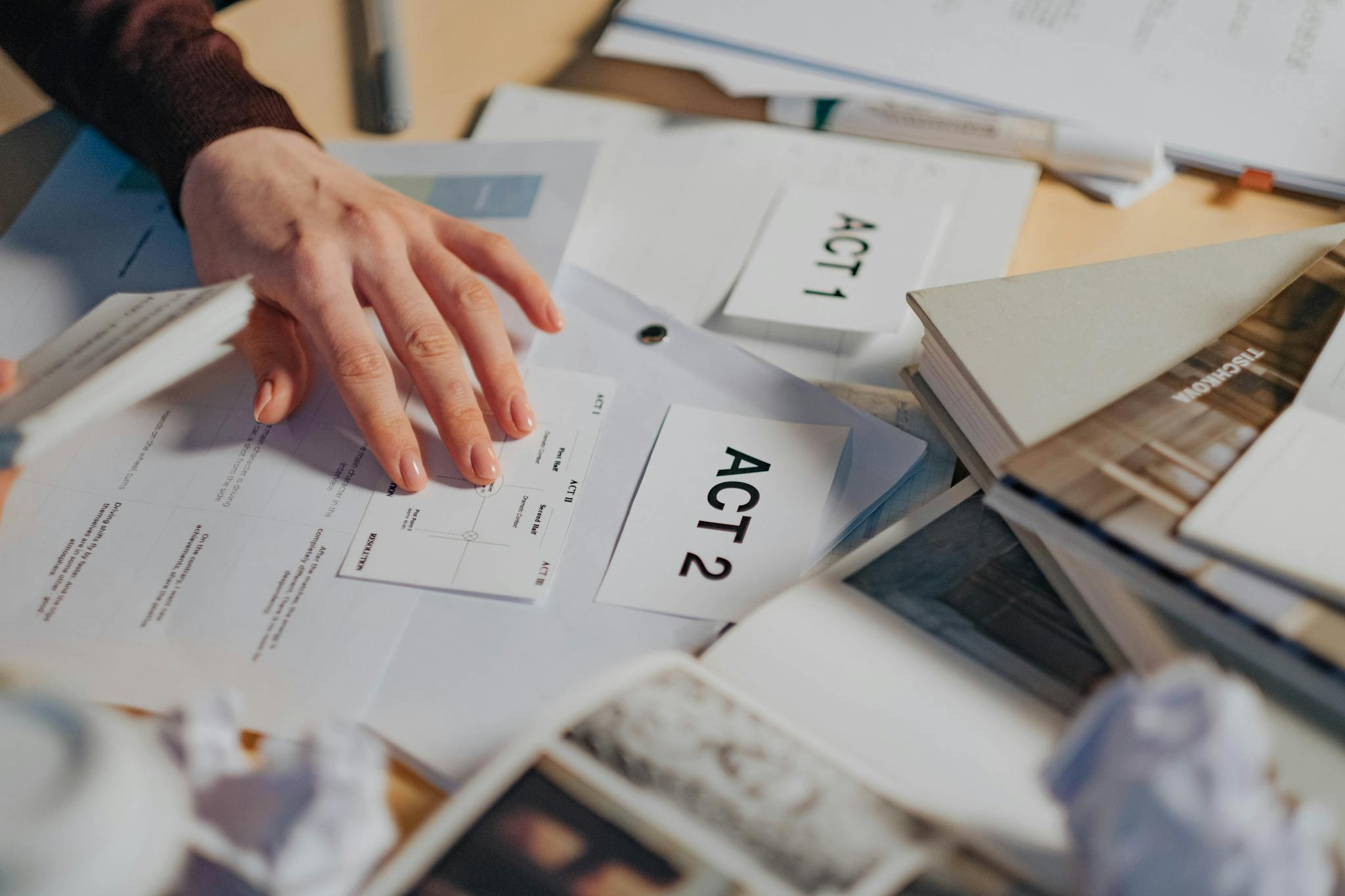 A cluttered desk with scripts, notes, and a person's hand organizing screenplay drafts.