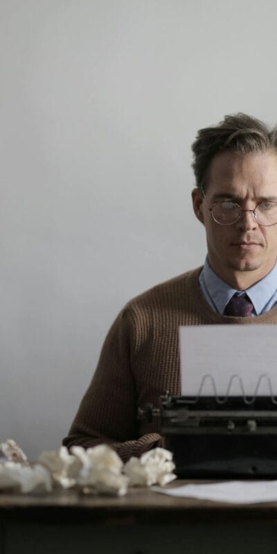 A thoughtful male writer typing on a vintage typewriter, surrounded by crumpled papers.