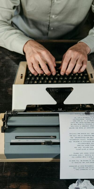 Hands typing on a vintage typewriter with papers and a coffee cup in view.